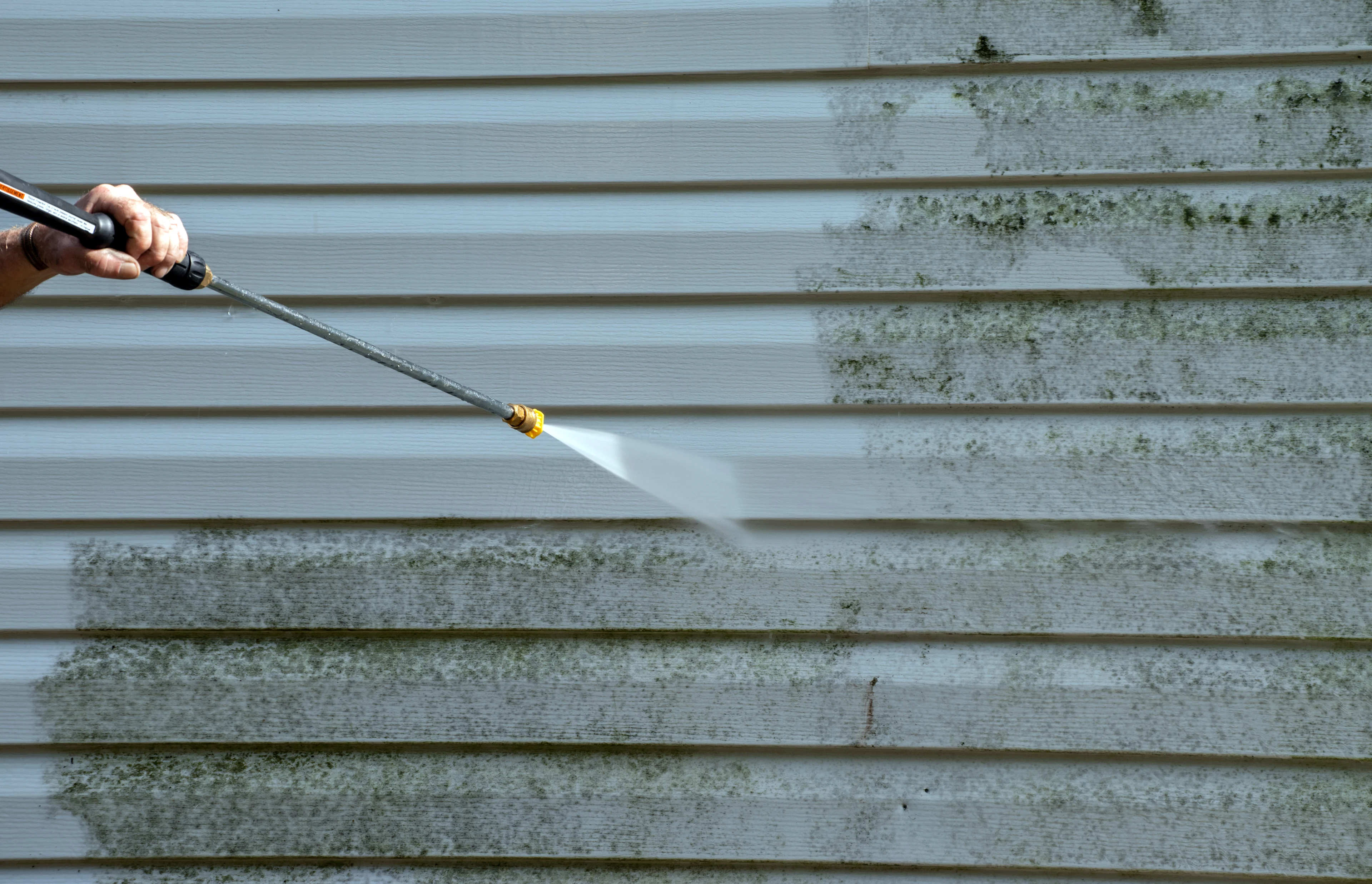 Pressure washer wand cleaning green algae off house siding