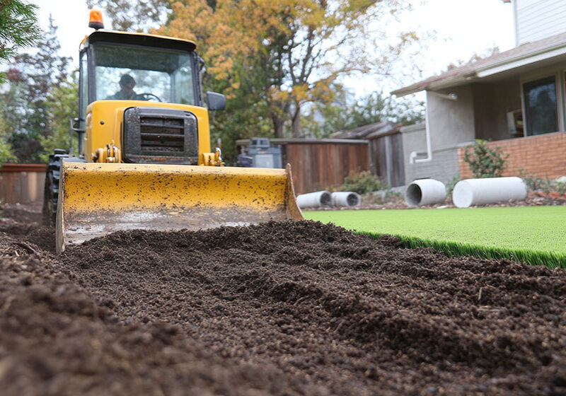 Yellow loader grading fresh soil beside a residential lawn