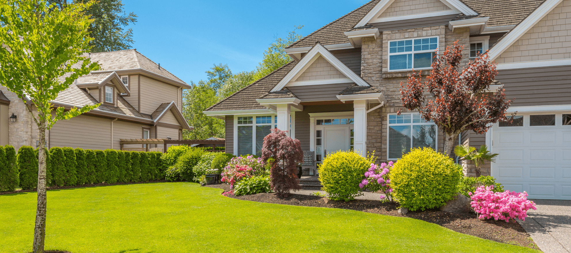 Bright green manicured lawn with shaped shrubs, flowering azaleas and clean mulch beds in front of a South Coast Massachusetts home